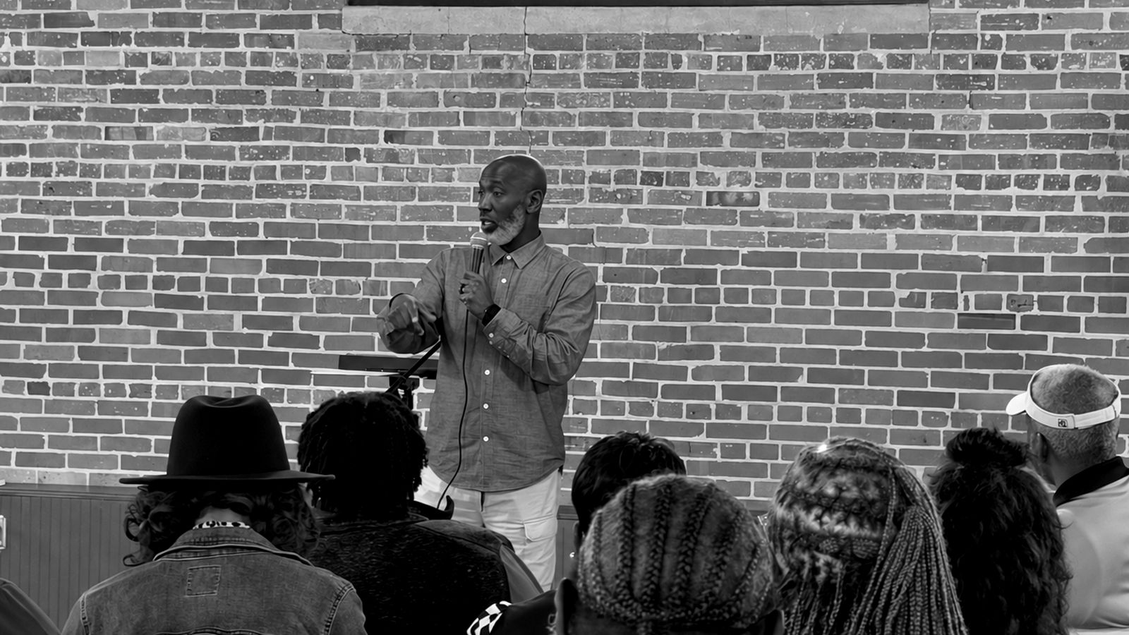A leader speaking with a microphone to a gathering in a brick-walled room