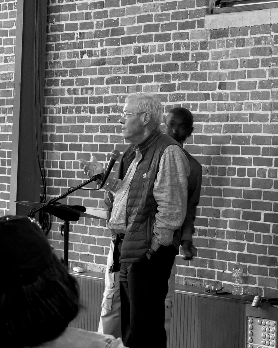 A community leader in a vest speaking at a microphone